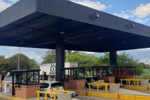 Se estima que para 2027 Colombia tendrá un sistema de peajes más automatizado Una estación de peaje al aire libre con marquesina negra, equipada con múltiples carriles y barreras bajo un cielo despejado.
