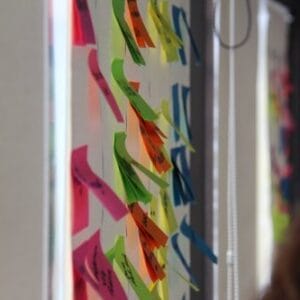 Coloridas notas adhesivas escritas en un tablero de vidrio transparente, vistas en ángulo, con un fondo borroso.