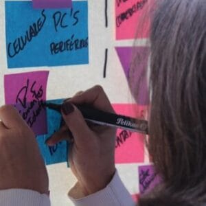 Una persona escribe en una nota adhesiva en una pared cubierta de post-its de colores, usando un marcador negro.