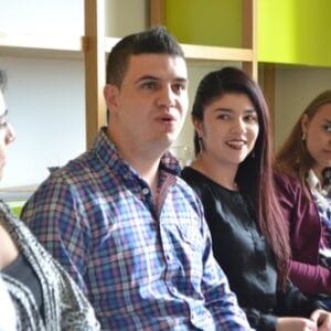 sittycia | TRABAJA CON NOSOTROS Cuatro personas sentadas en una reunión escuchan atentamente a un orador fuera de cámara. parecen comprometidos e interesados en la discusión.