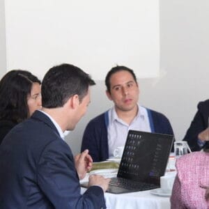 Un grupo de cinco profesionales, entre ellos tres hombres y dos mujeres, participaban en una reunión de negocios en una mesa con ordenadores portátiles y documentos.