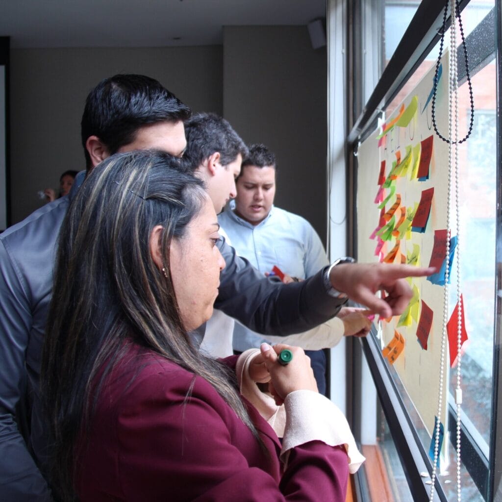 Un grupo de profesionales participando en una sesión de lluvia de ideas colaborativa utilizando notas adhesivas en una ventana en una habitación bien iluminada.