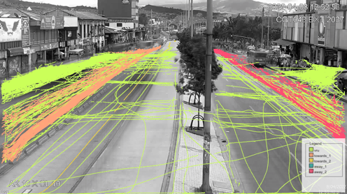 Análisis de tráfico en una calle de la ciudad que muestra líneas de trayectoria coloreadas que siguen el movimiento de los vehículos, capturadas por una cámara CCTV en blanco y negro.