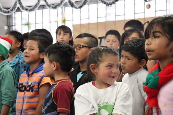 Grupo de niños de distintas edades y apariencias parados juntos, luciendo comprometidos, con decoraciones festivas de fondo.