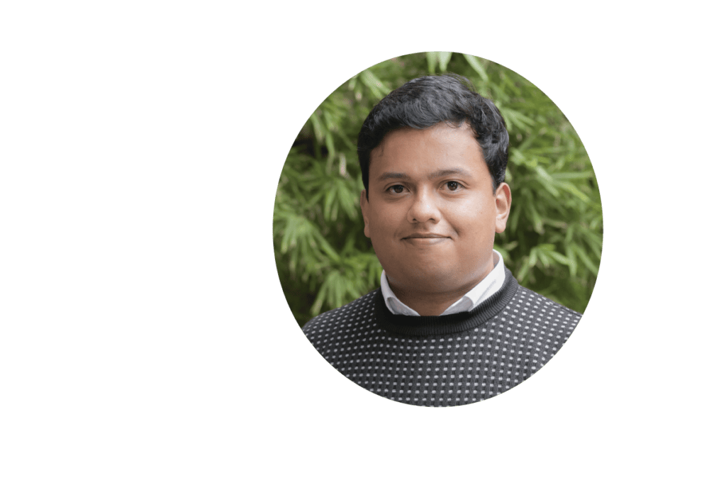 Retrato de un joven con el pelo corto y oscuro, vestido con una camisa estampada en blanco y negro, sonriendo levemente, sobre un fondo de follaje verde borroso.