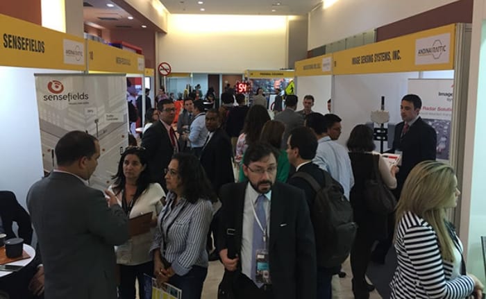 Personas haciendo networking en una concurrida feria comercial con varios stands de empresas visibles al fondo.