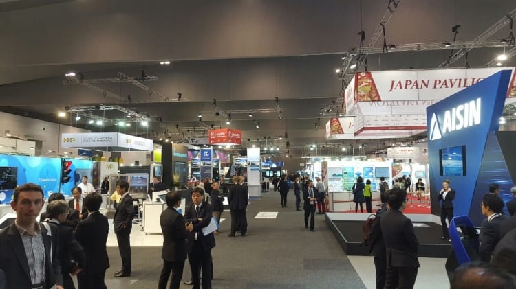 Amplia vista de una concurrida feria comercial con varios stands corporativos, en los que destaca el letrero "pabellón de Japón". asistentes y expositores interactúan.