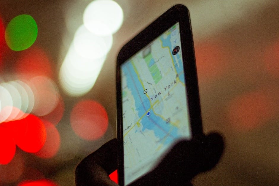 Primer plano de una mano que sostiene un teléfono inteligente que muestra un mapa de la ciudad de nueva york, con coloridas luces bokeh de fondo.