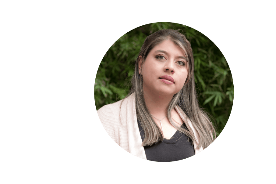 Una mujer con cabello de longitud media y un pañuelo mira hacia un lado, contra un fondo de follaje verde borroso.