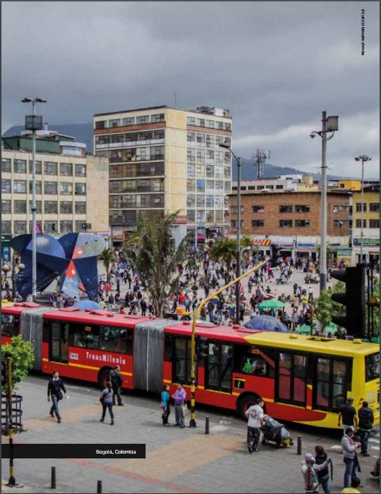 Una animada escena urbana en bogotá, colombia, con una multitud de personas, un autobús transmilenio rojo y amarillo y edificios modernos bajo un cielo nublado.