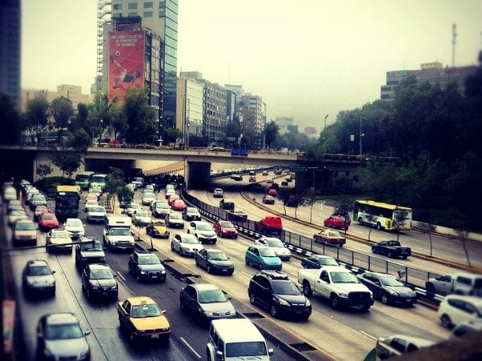 Una transitada autopista urbana de varios carriles con vehículos en movimiento y estacionarios, cielo nublado y edificios de gran altura circundantes.
