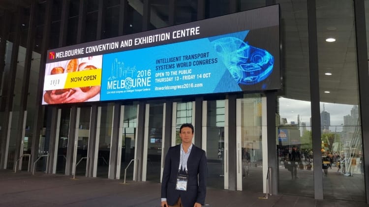 Un hombre parado frente al centro de convenciones y exposiciones de Melbourne, que muestra carteles que promocionan diversos eventos.