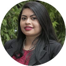 Retrato de una mujer sonriente con el pelo largo y negro, vestida con una chaqueta negra y una blusa roja, sobre un fondo de hojas verdes.