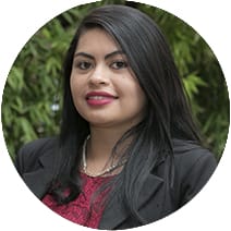 Retrato de una mujer sonriente con el pelo largo y negro, vestida con una chaqueta negra y una blusa roja, sobre un fondo de hojas verdes.