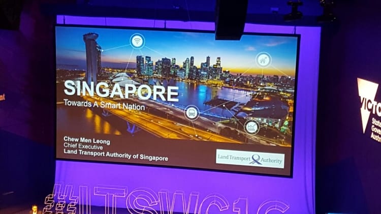 Pantalla de proyección que muestra una presentación sobre "Singapur: hacia una nación inteligente" en una conferencia, con una imagen de un paisaje urbano de fondo.