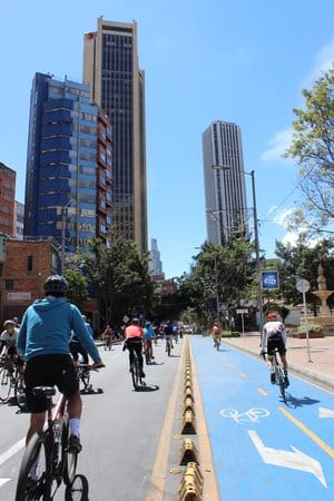 Ciclistas que viajan por un carril bici designado en un día soleado con altos edificios de la ciudad al fondo.