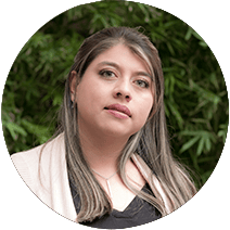 Retrato de una mujer pensativa con cabello largo y maquillaje neutro, mirando hacia otro lado, con follaje verde al fondo.