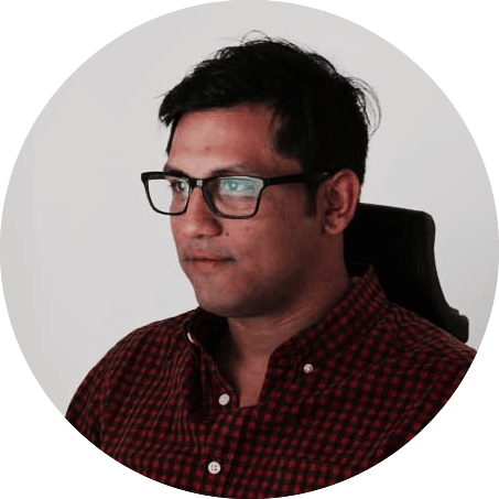 Hombre con gafas y camisa a cuadros roja, mirando hacia un lado con una expresión pensativa, sobre un fondo neutro.