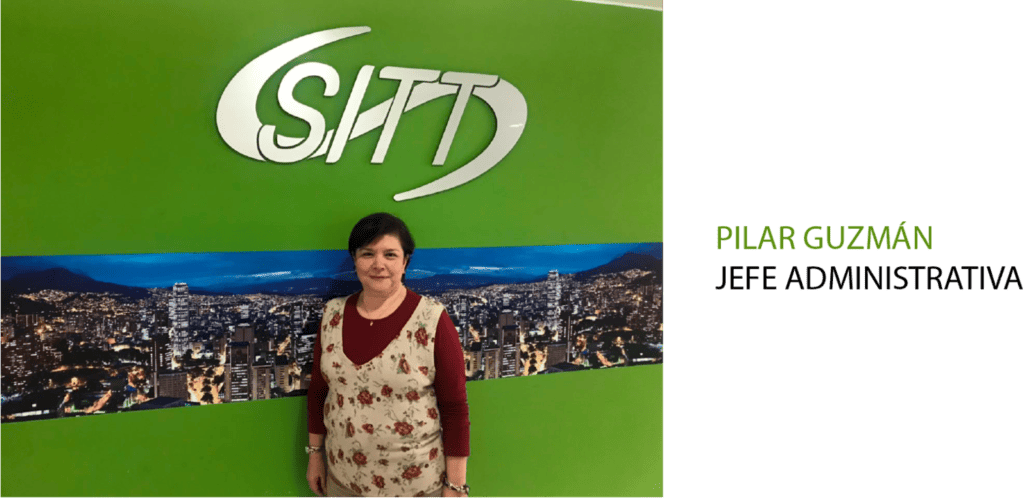 Mujer parada frente a una pared verde con el logo "sitt" y un fondo de paisaje urbano, llamada pilar guzmán.