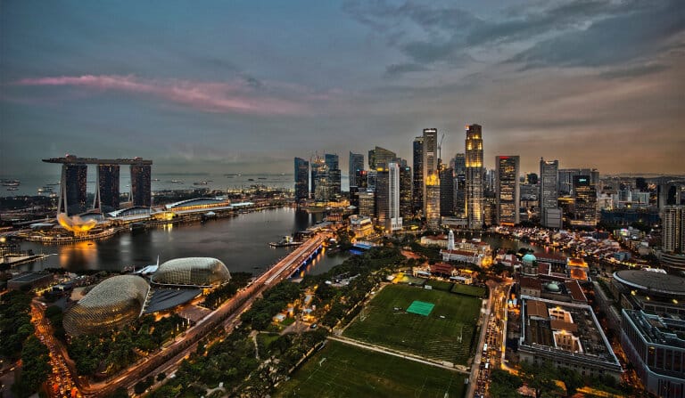 Vista aérea del horizonte de Singapur al anochecer, con arenas de Marina Bay, rascacielos y luces iluminadas de la ciudad.